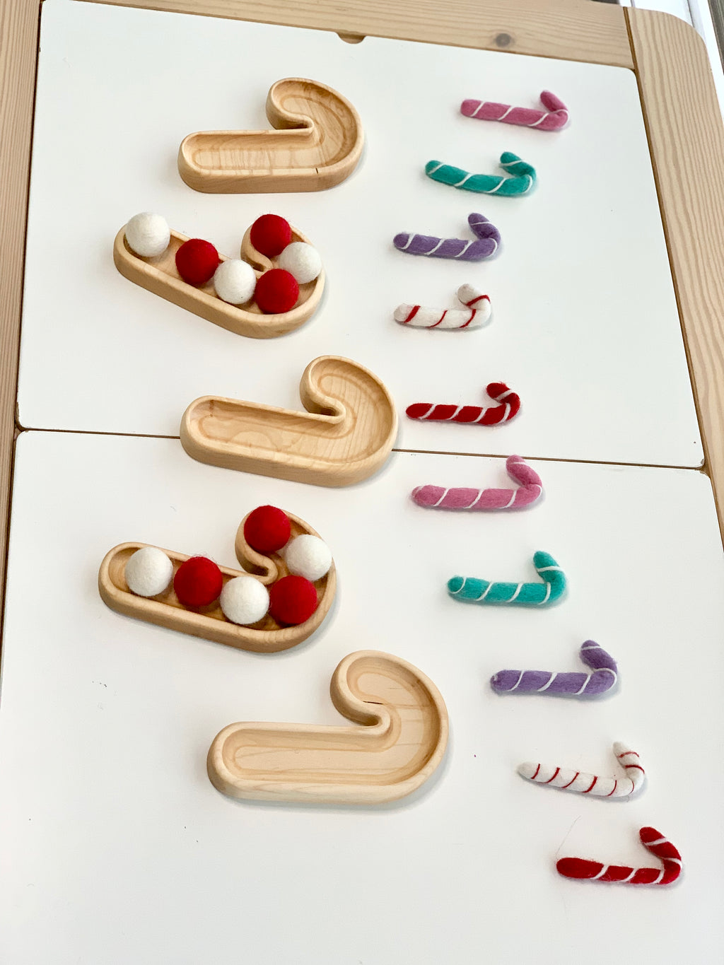 Natural wooden candy cane-shaped plates paired with colorful felt candy cane and pom poms on white surface