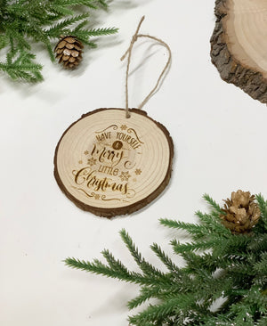 Round wooden Christmas ornament with bark edge and engraved cursive text "Have yourself a Merry little Christmas" with pine cones and evergreen branches