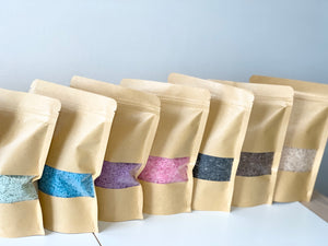 Kraft paper resealable bags filled with colourful sensory bin fillers in various shades on white surface