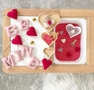 Natural wood nesting heart plates arranged with Valentine-themed sensory items on wooden tray background