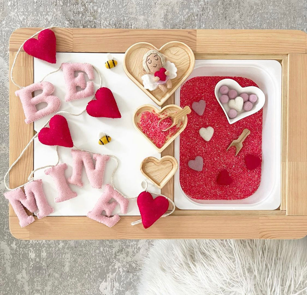 Natural wood nesting heart plates arranged with Valentine-themed sensory items on wooden tray background