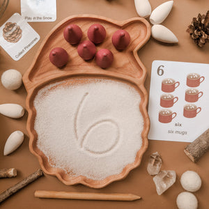Wooden Santa-shaped sensory tray filled with white sand and six red cone pieces surrounded by natural sensory items and flashcards