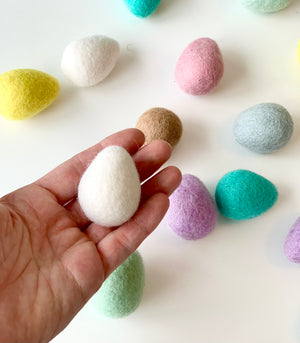 Hand holding one white felt Easter egg surrounded by colorful handmade wool felt eggs on white background