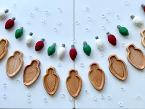 Light bulb shaped natural wooden sensory trays arranged in a row with red, green, and white felted bulbs on white background