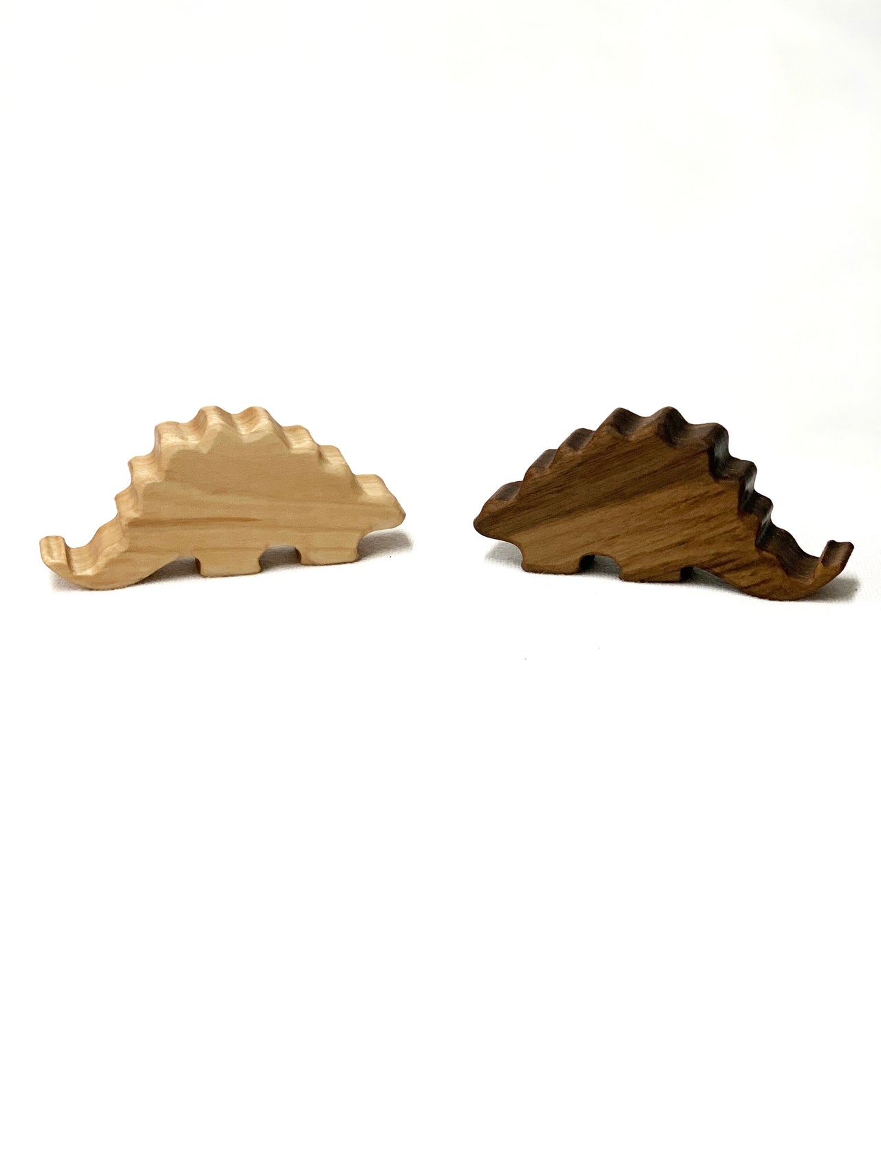 Two small wooden Stegosaurus dinosaur toy figurines in light and dark wood on white background