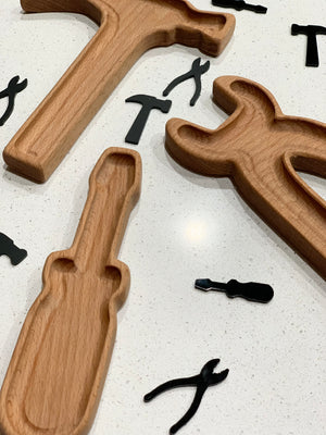 Wooden tool-shaped sensory trays with cutouts and small black tool-shaped pieces on white speckled surface