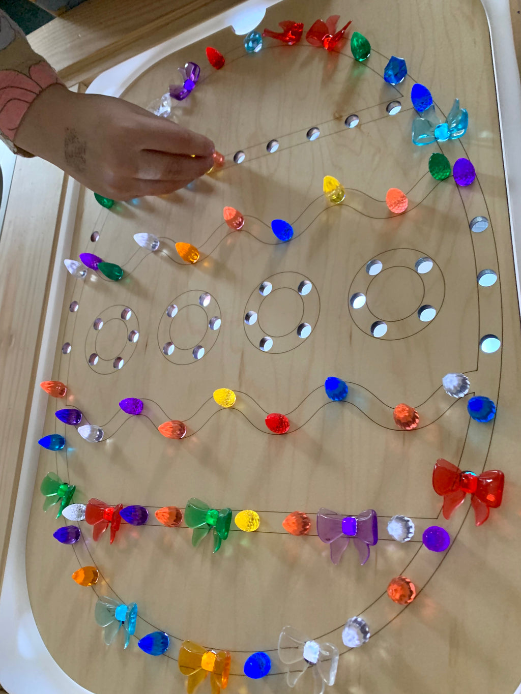 Wooden Easter egg-shaped insert with colorful translucent pegs being placed by hand on light wood surface
