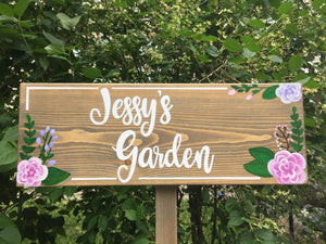 Personalized wooden garden sign with white cursive lettering and pink and purple floral accents on natural wood grain background