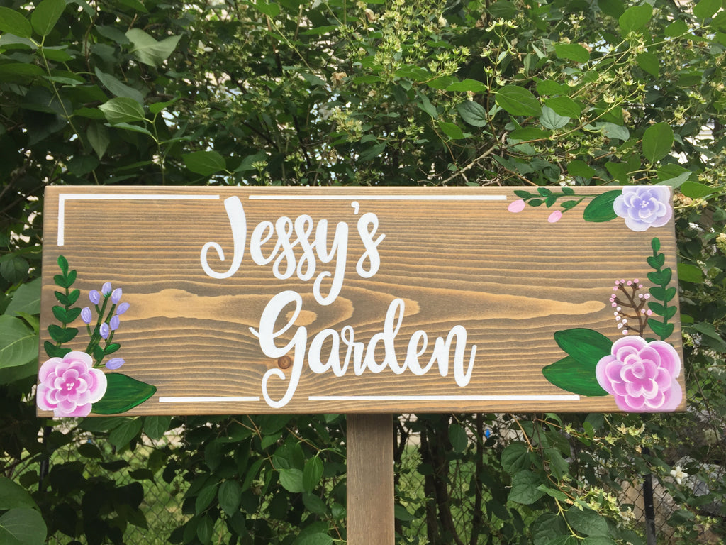 Personalized wooden garden sign with white cursive lettering and pink and purple floral accents on natural wood grain background