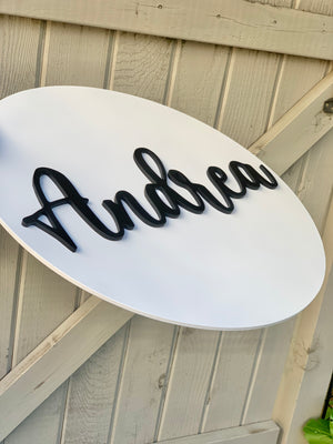 3D round white sign with black cursive name Andrea mounted on wood panel background