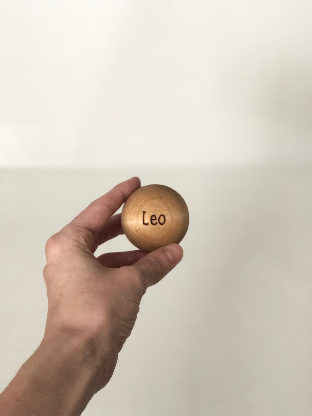 Hand holding a wooden extra ball for bowling set with the name Leo engraved on it against a plain background