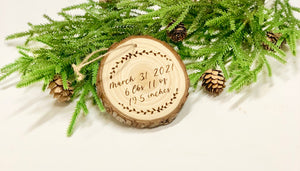 Wood burned wooden baby’s first Christmas ornament with birth details surrounded by pine branches and pinecones