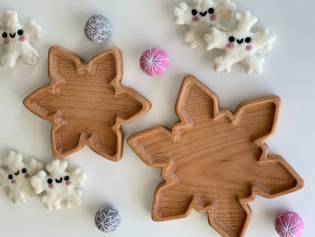 Two natural wooden snowflake-shaped plates surrounded by small felt snowflake figures and decorative balls