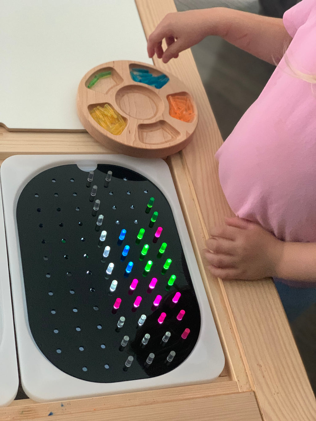 Child placing colorful peg add-ons into small holes on geometric light board Flisat tabletop insert