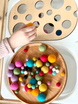 Child’s hand placing a felt ball into wooden Circle Ball Sorter Flisat table top insert with natural wood tray of colorful felt balls