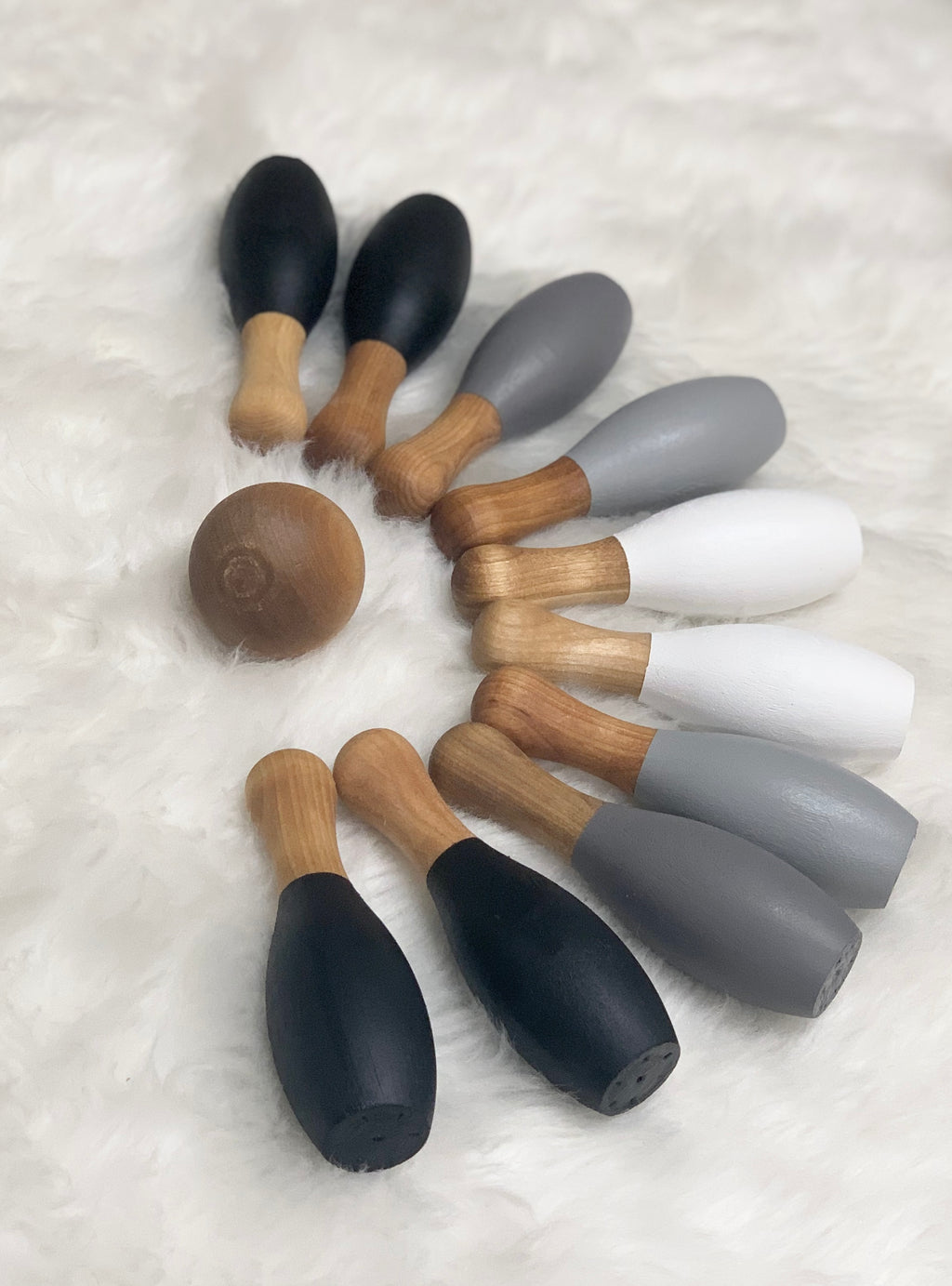 Monochrome wood bowling set with ten pins in black, gray, and white, and a natural wood ball on soft white background