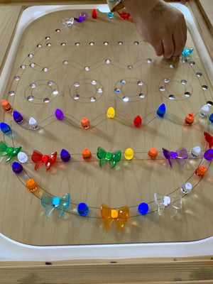 Wooden Flisat tray shaped like an Easter egg with colorful light-up pegs inserted in holes on table surface