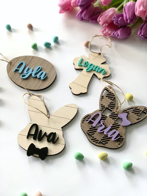 Custom wooden Easter basket name tags with pastel-colored names in script and bunny and cross shapes on light wood background