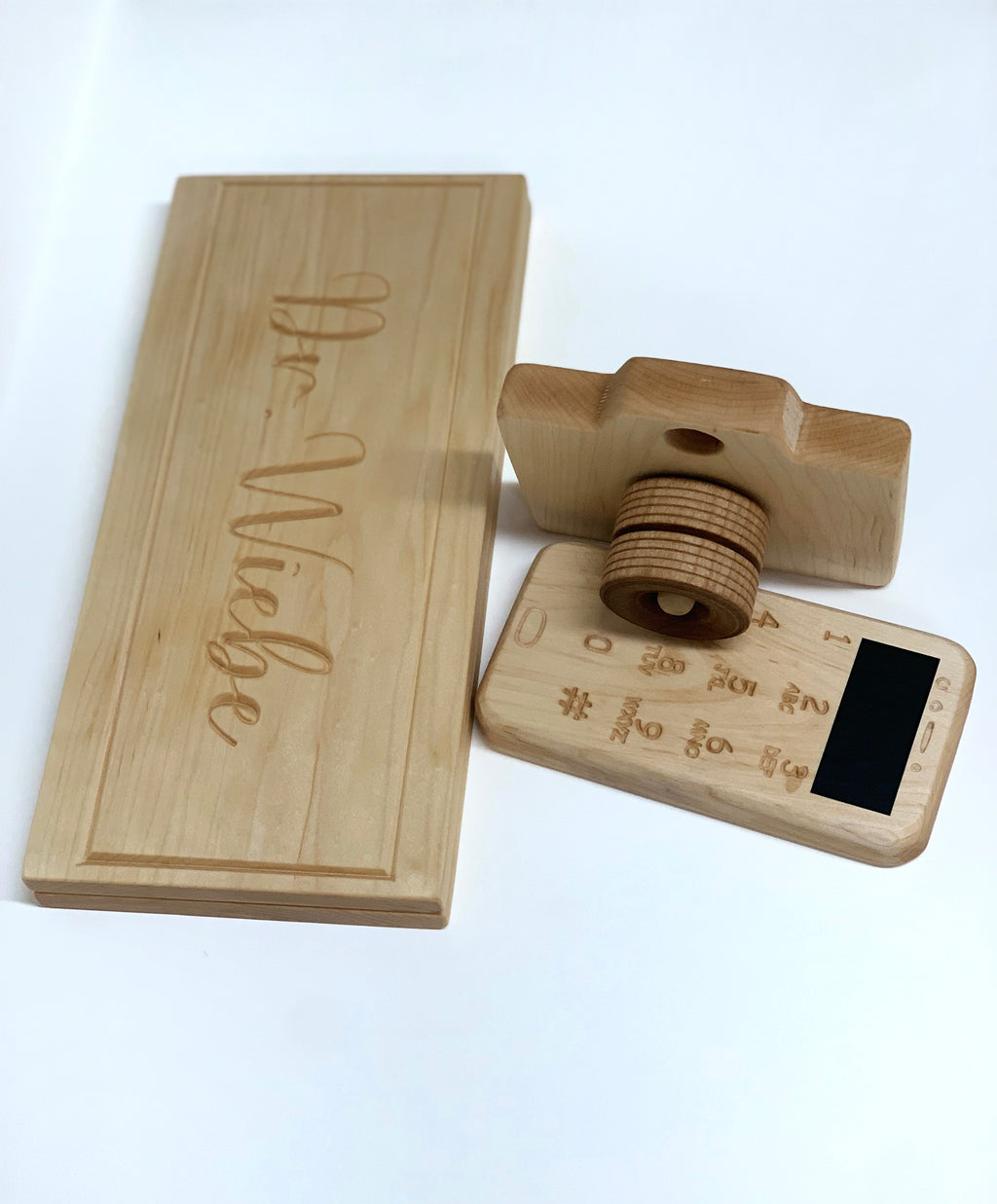 Natural wooden toy laptop with engraved keyboard and small wooden camera on white background next to engraved name plaque