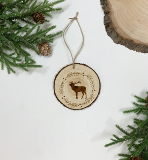 Round wood Christmas ornament with wood burned deer and decorative wreath design hanging with twine on white background