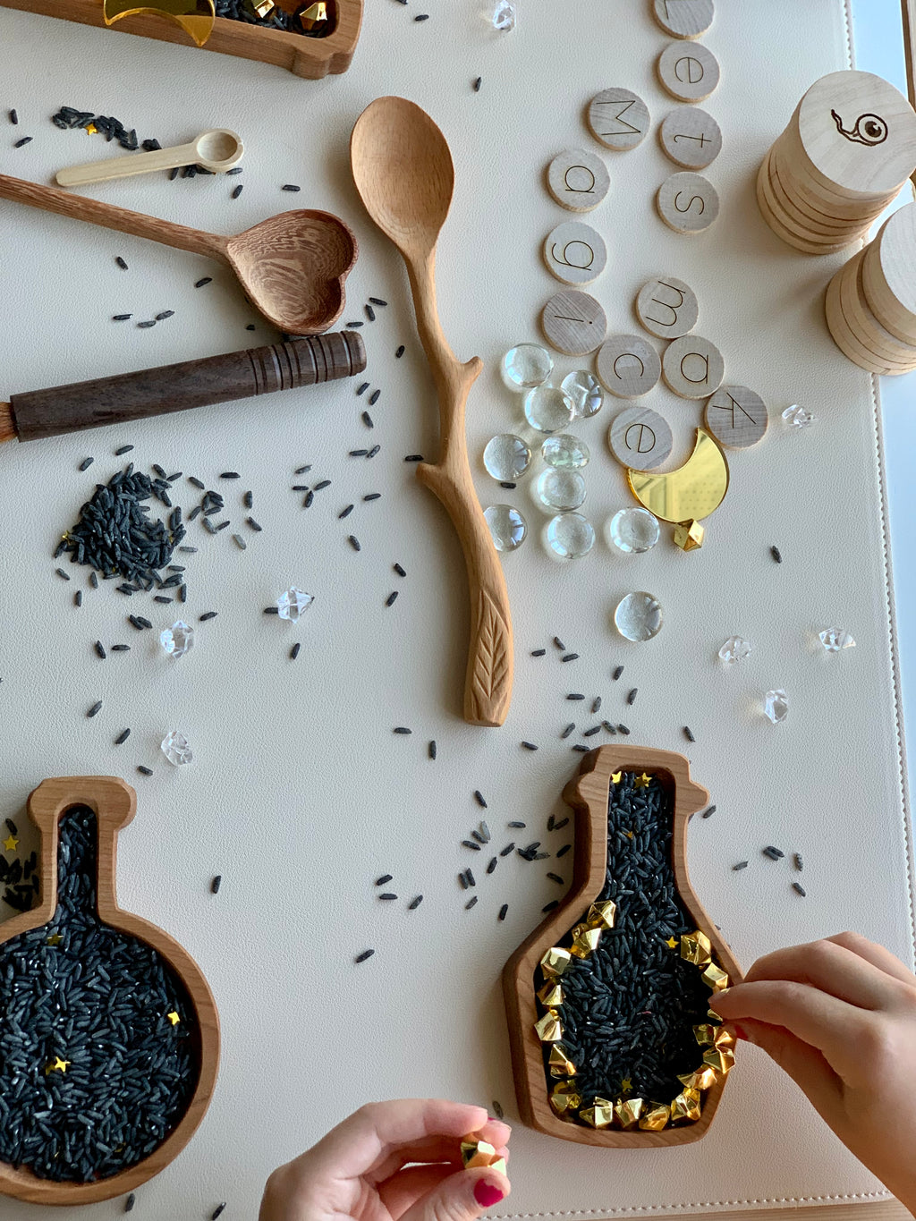 Hand-carved wooden spoon with twig and leaf design on natural wood grain background near wooden toys and black rice grains