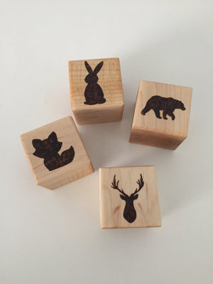 Natural wooden 1.5 inch blocks with engraved animal silhouettes including rabbit, bear, fox, and deer on light wood background