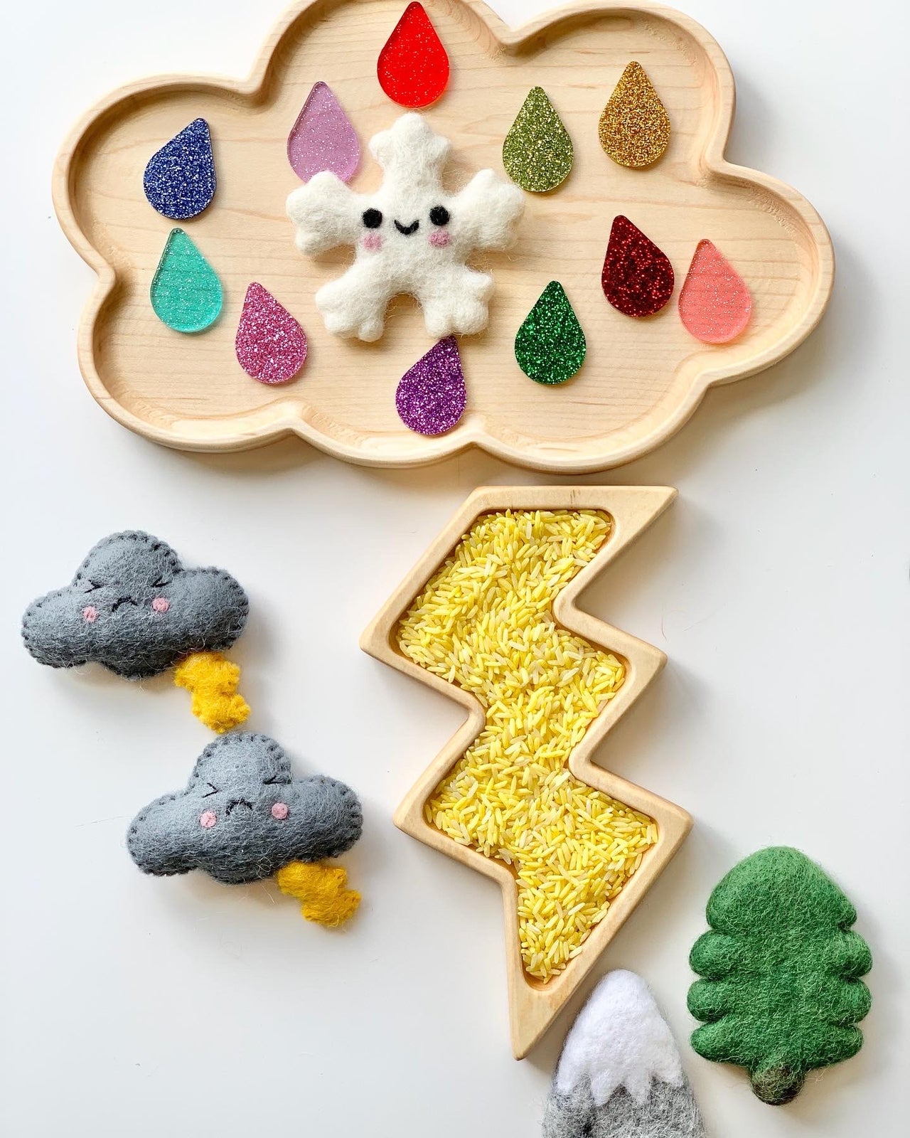 Wooden cloud-shaped sensory tray with colorful raindrop pieces, felt snowflake, lightning plate filled with yellow rice, and felt weather shapes
