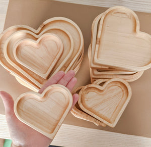 Natural wooden nesting heart plates and sensory trays stacked and held in hand on light wood surface