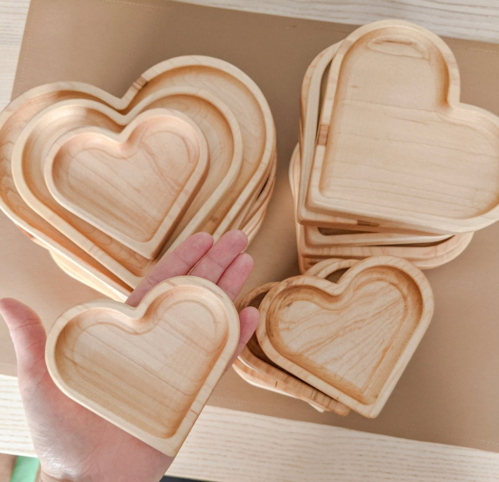 Natural wooden nesting heart plates and sensory trays stacked and held in hand on light wood surface