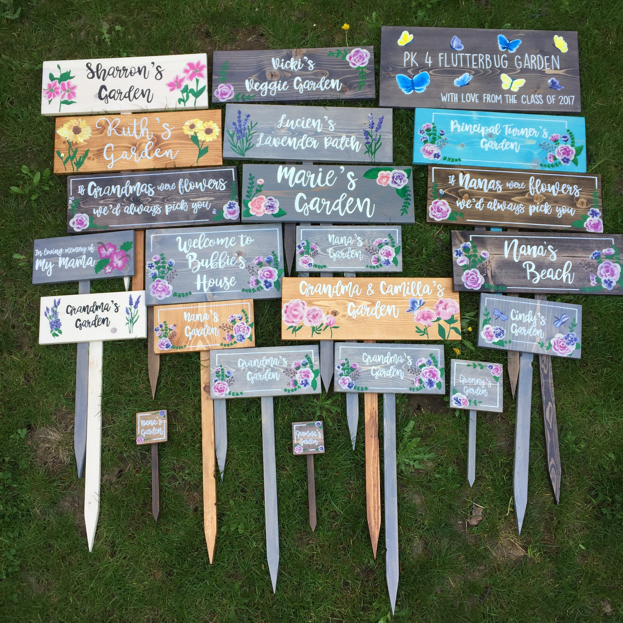 Assorted large personalized wooden garden signs with painted flowers and handwritten style white letters on colorful backgrounds