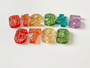 Rainbow glitter resin numbers set 0 to 9 with various bright colors on white background