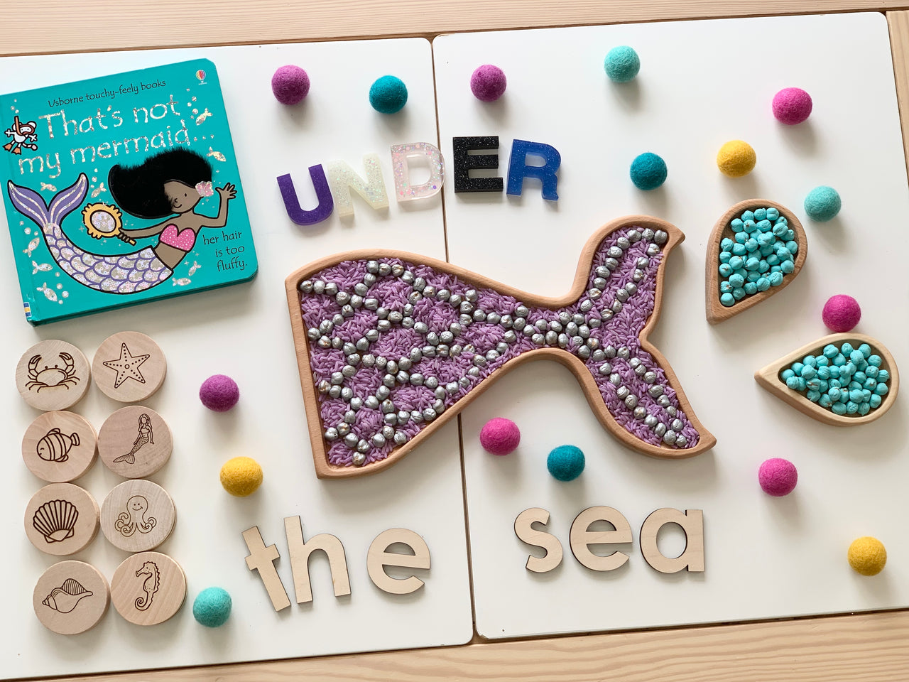 Montessori-inspired mermaid memory game with wood discs, textured whale pieces, colorful felt balls, and children's book on white surface