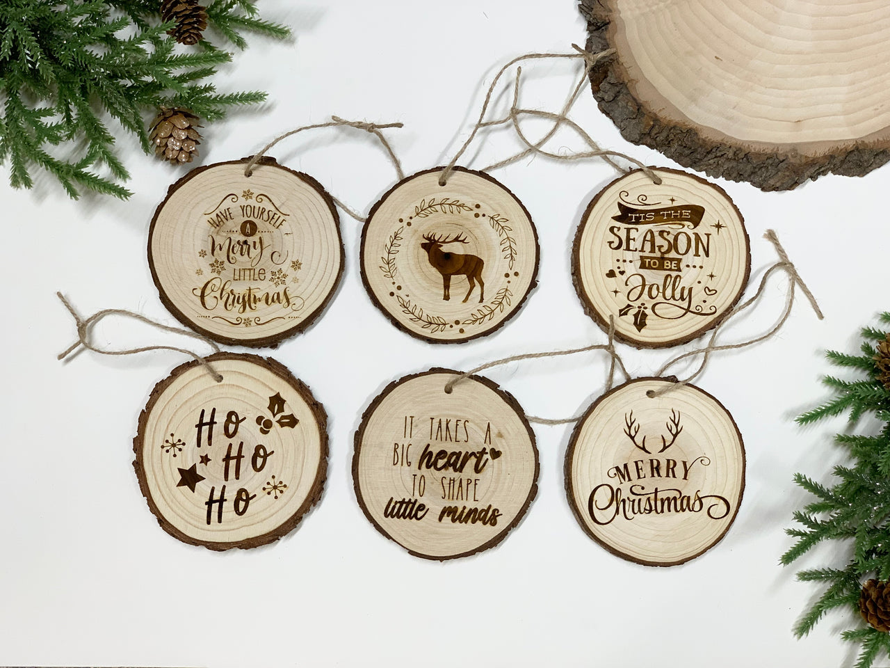 Set of six round wood burned Christmas ornaments with festive phrases and a reindeer illustration on natural wood slices