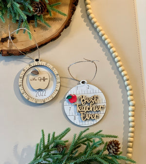 Two round wooden Christmas ornaments with ruler design, one with red apple and "Best teacher ever" text, the other engraved with apple and name