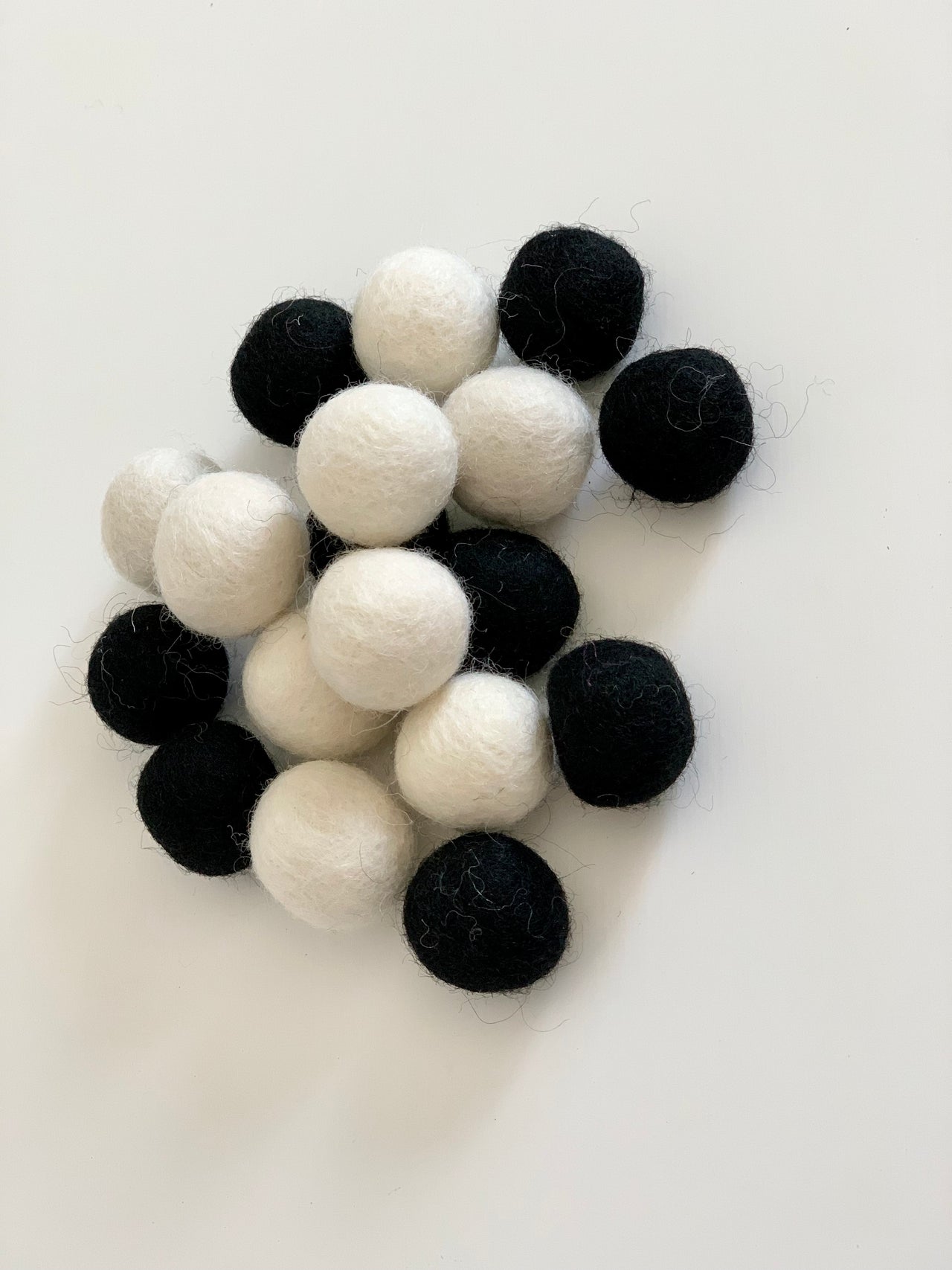 Assortment of black and white felt balls scattered on a white surface with soft wool texture visible
