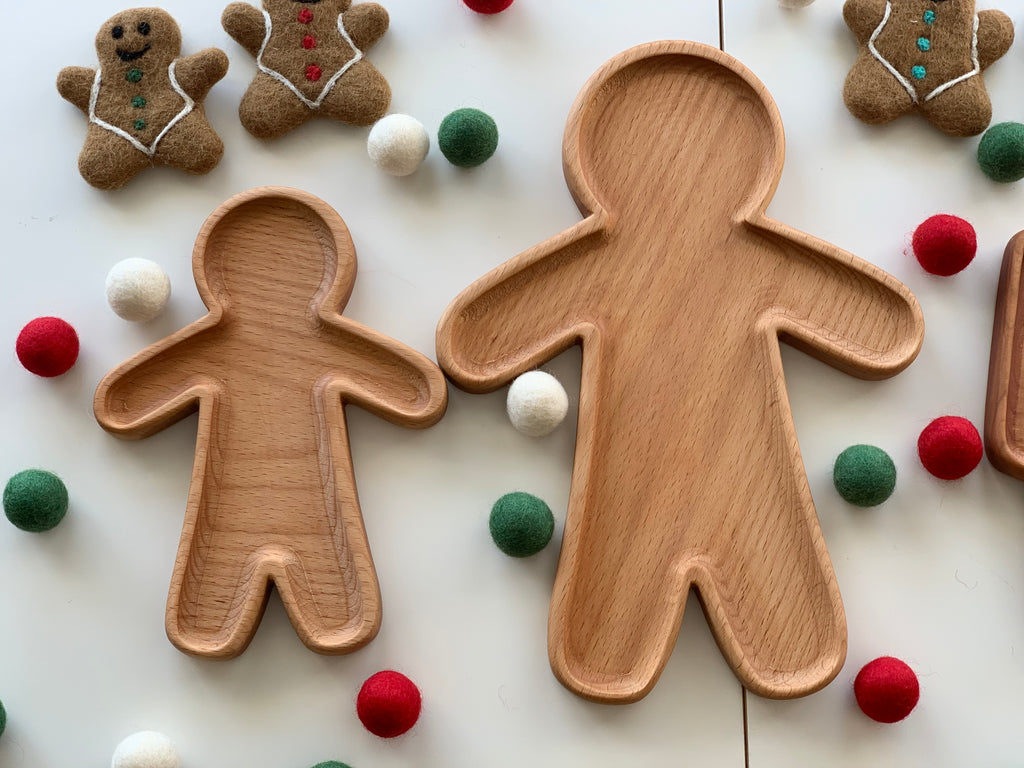Two natural wooden person-shaped sensory trays with smooth carved edges on white surface with felt balls and gingerbread decorations