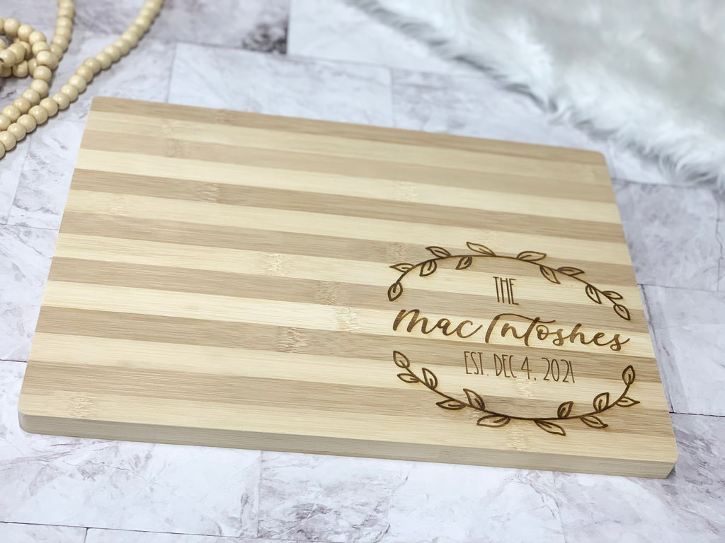 Natural striped bamboo serving board with personalized engraved wreath and custom name and date design on corner