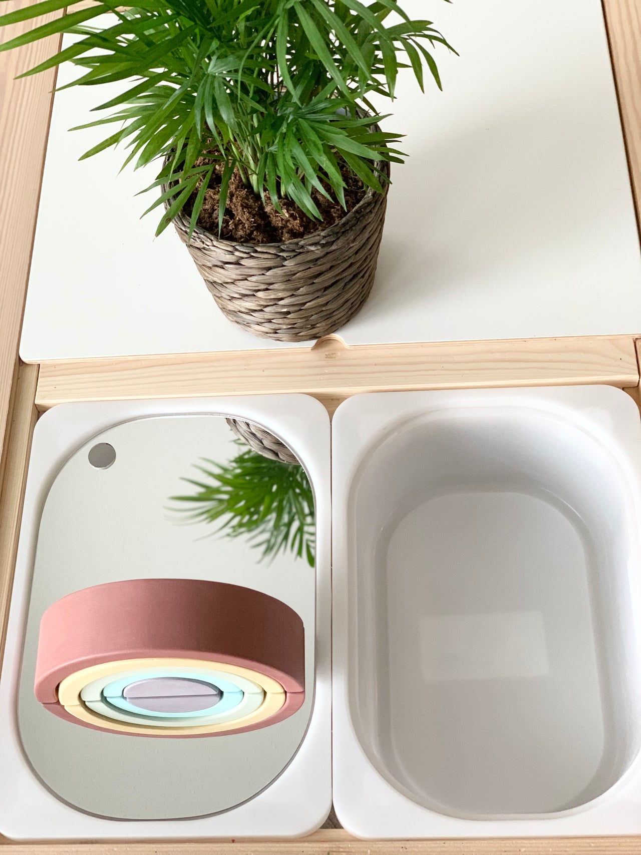 Small Flisat bin with premium mirrored acrylic table insert reflecting plant and wooden rainbow toy on white wood surface