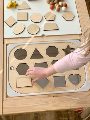 Child placing wooden rectangle piece into shape sorter Flisat table top insert with various geometric shapes on wooden table