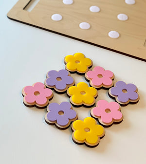 Wooden flower-shaped cookie pieces in pink, purple, and yellow with a cookie sheet in the background on white surface