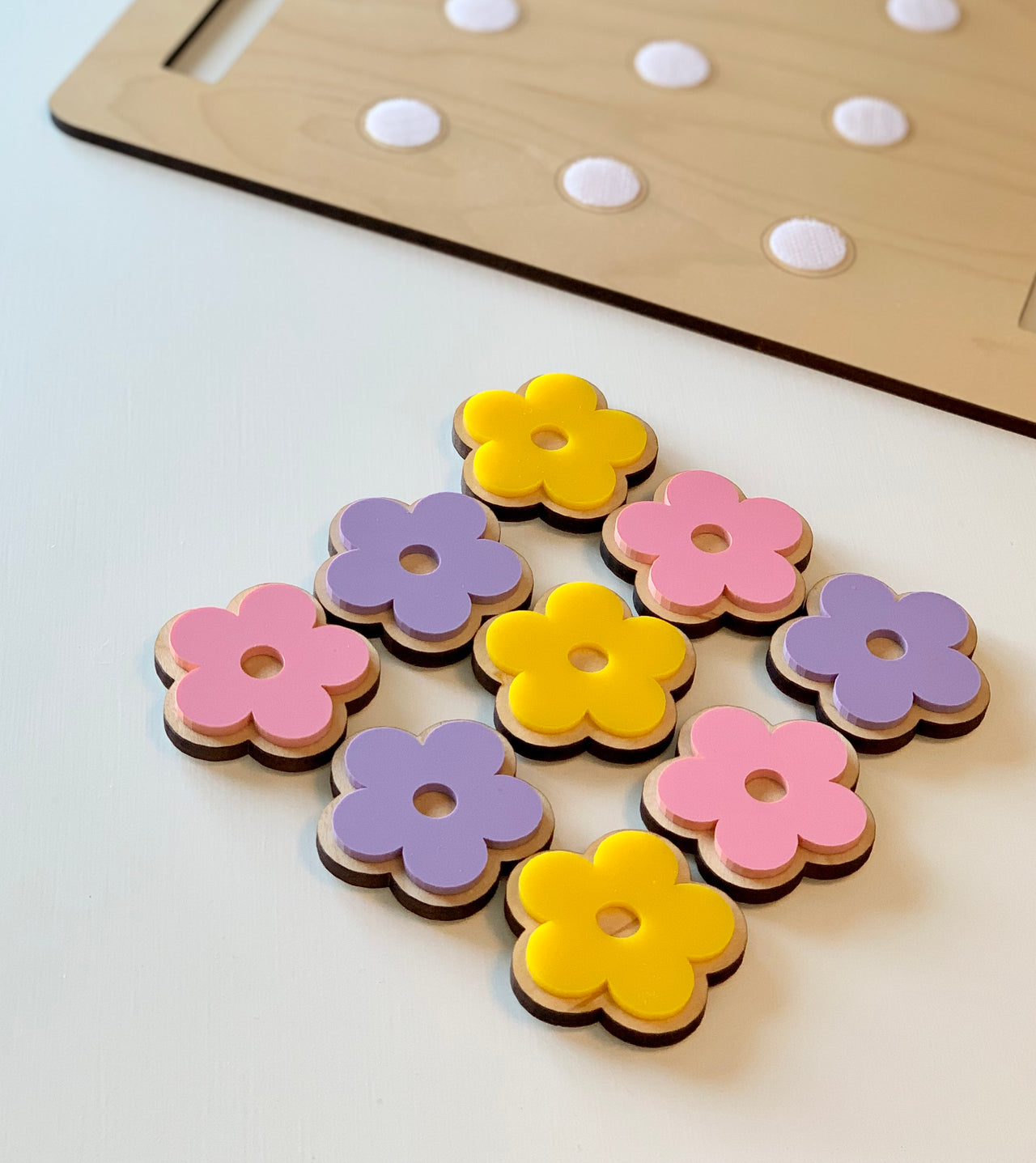 Wooden flower-shaped cookie pieces in pink, purple, and yellow with a cookie sheet in the background on white surface