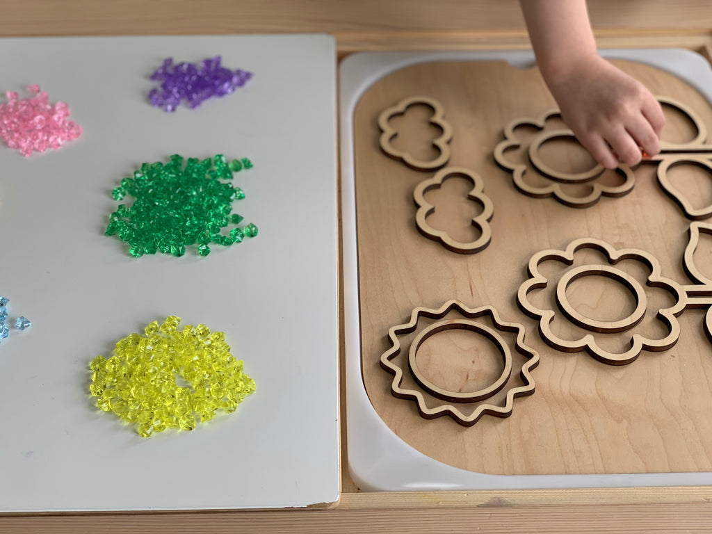 Assorted mini acrylic treasure gems in yellow, green, purple, pink, and blue next to wooden flower and cloud puzzle pieces on table