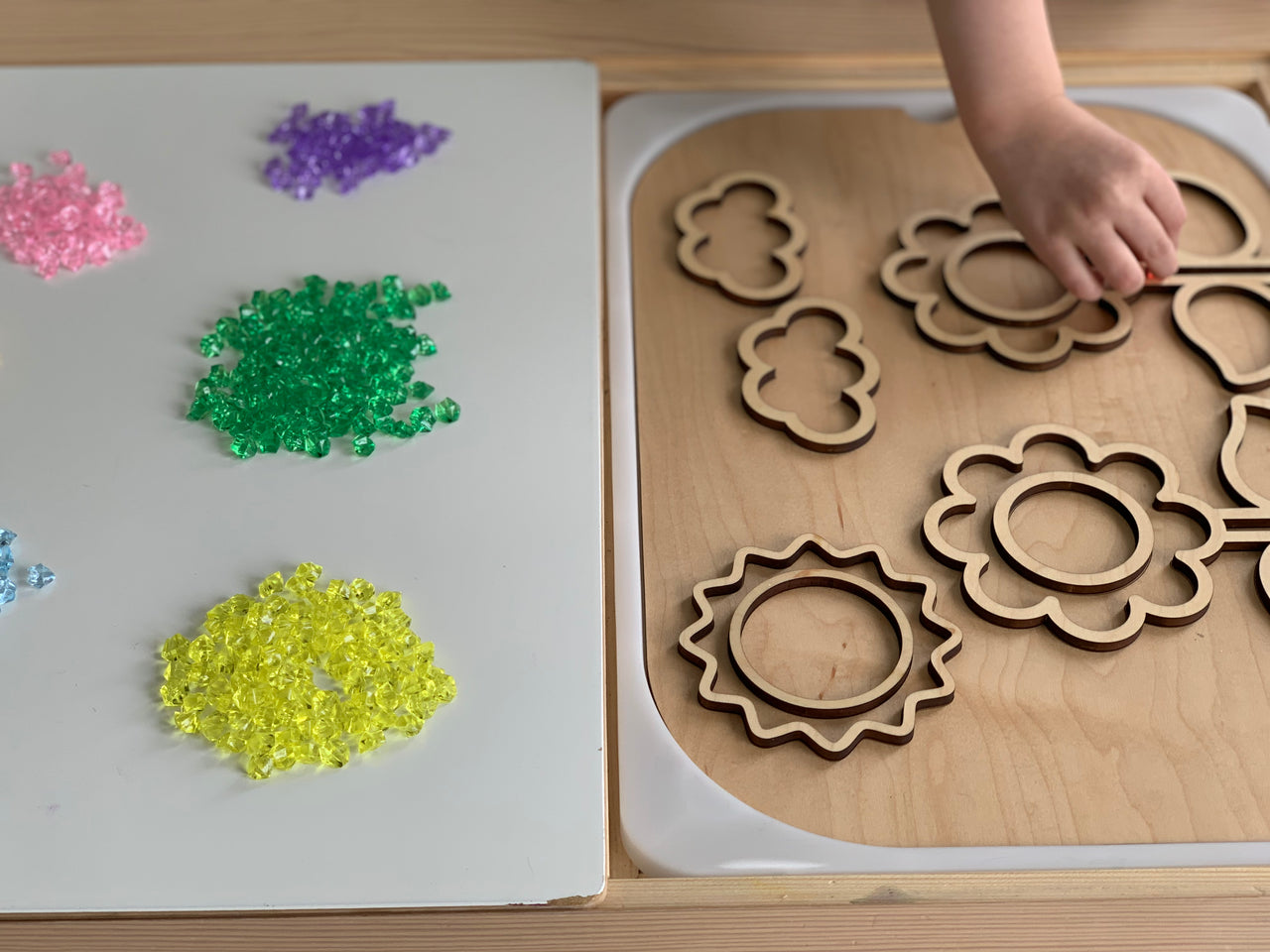 Assorted mini acrylic treasure gems in yellow, green, purple, pink, and blue next to wooden flower and cloud puzzle pieces on table