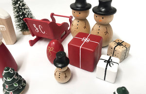 Hand-painted wooden Christmas peg dolls including snowmen, presents, sleigh, and festive trees on white background