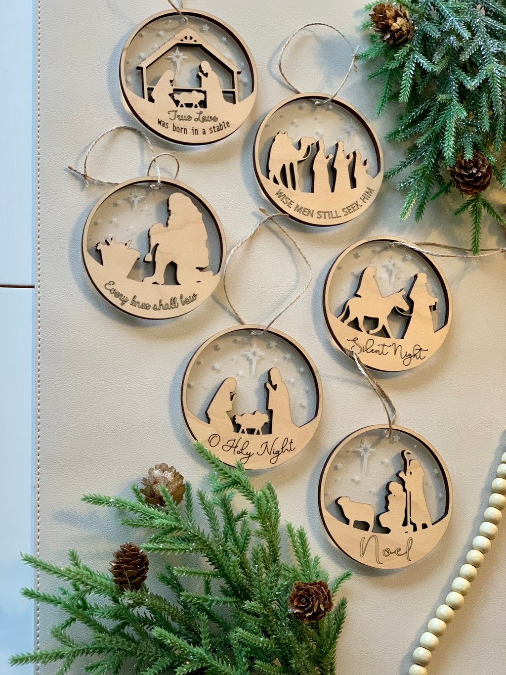 Set of two-layer wood and acrylic nativity Christmas ornaments with religious scenes and festive greenery background