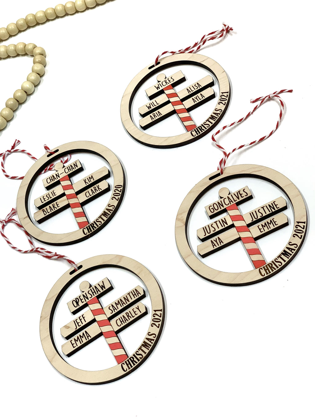 Round wooden North Pole family Christmas ornaments with red and white striped signposts and personalized names on white background