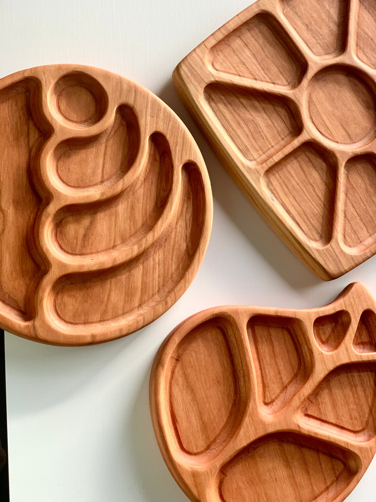 Set of natural wooden sensory trays in wave circle, floral, and fish shapes with multiple compartments on white surface