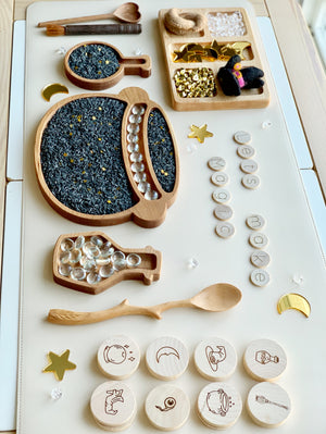 Twig shaped wooden spoon with carved handle placed on a white surface with various wooden trays and tokens