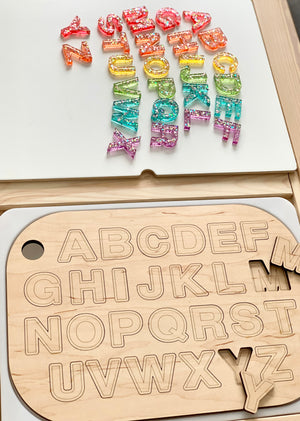 Wooden uppercase alphabet puzzle board with colorful resin lowercase letters scattered on white surface above it