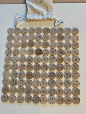 Set of 100 laser engraved wooden number discs from 1 to 100 arranged in rows with drawstring cloth bag on white surface